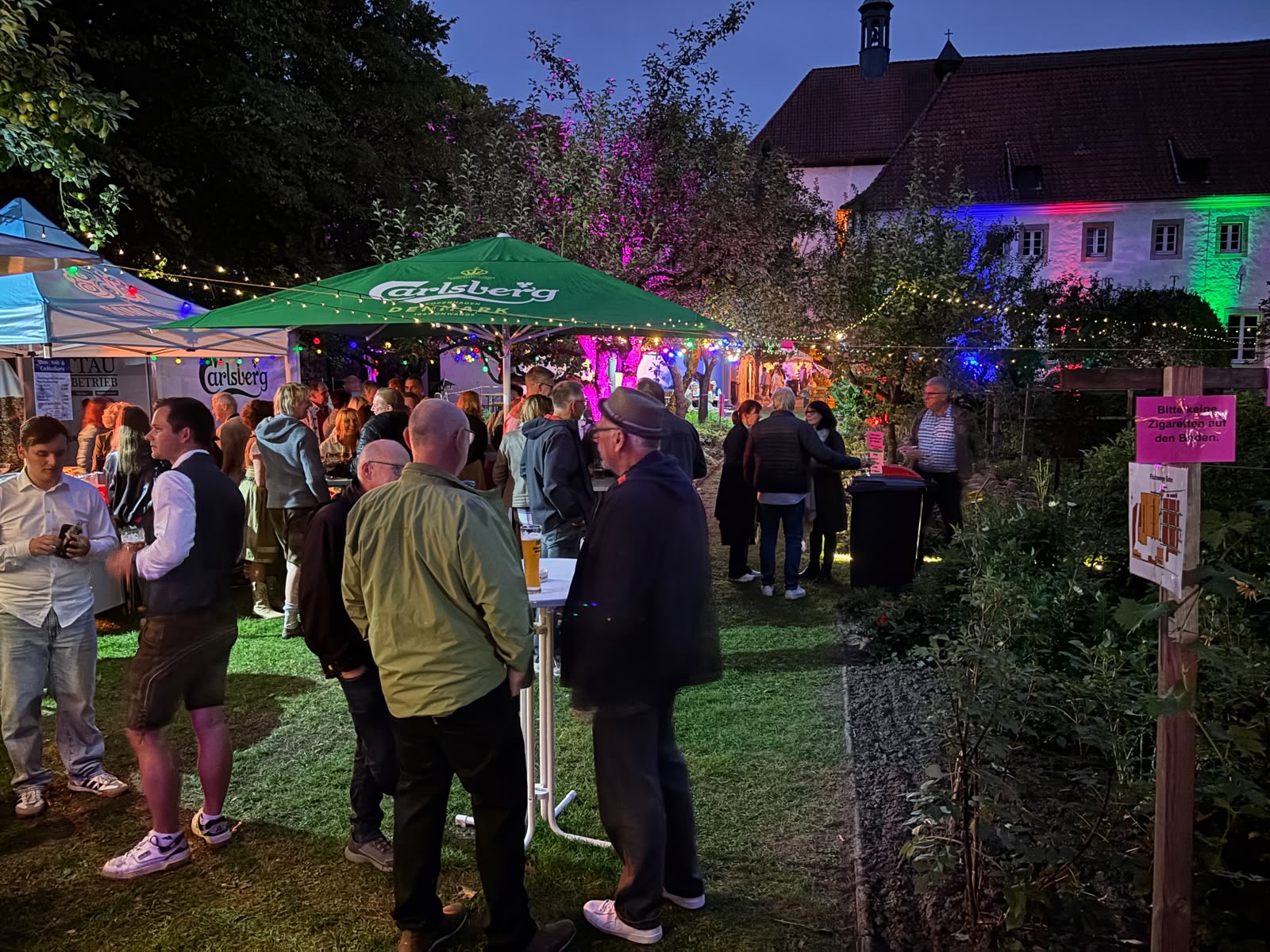 Gäste des Oktoberfestes im beleuchteten Klostergarten